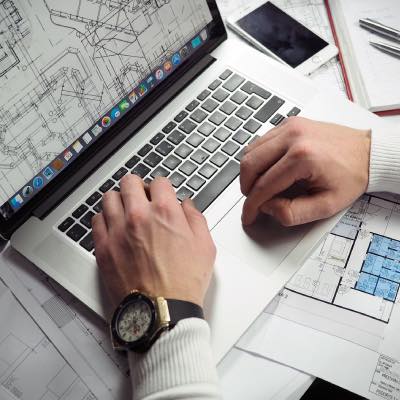 Hands of person working on a laptop showing plans on the screen
